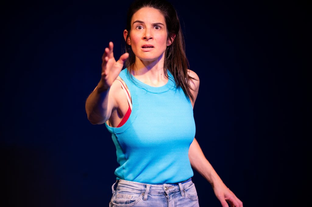 A woman with dark hair reaches forward. She is wearing a blue top and jeans