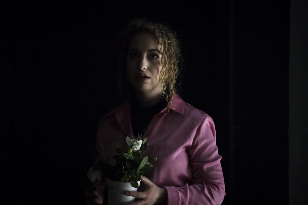 A woman in a pink shirt holding a potted plant. Her face is half covered in darkness